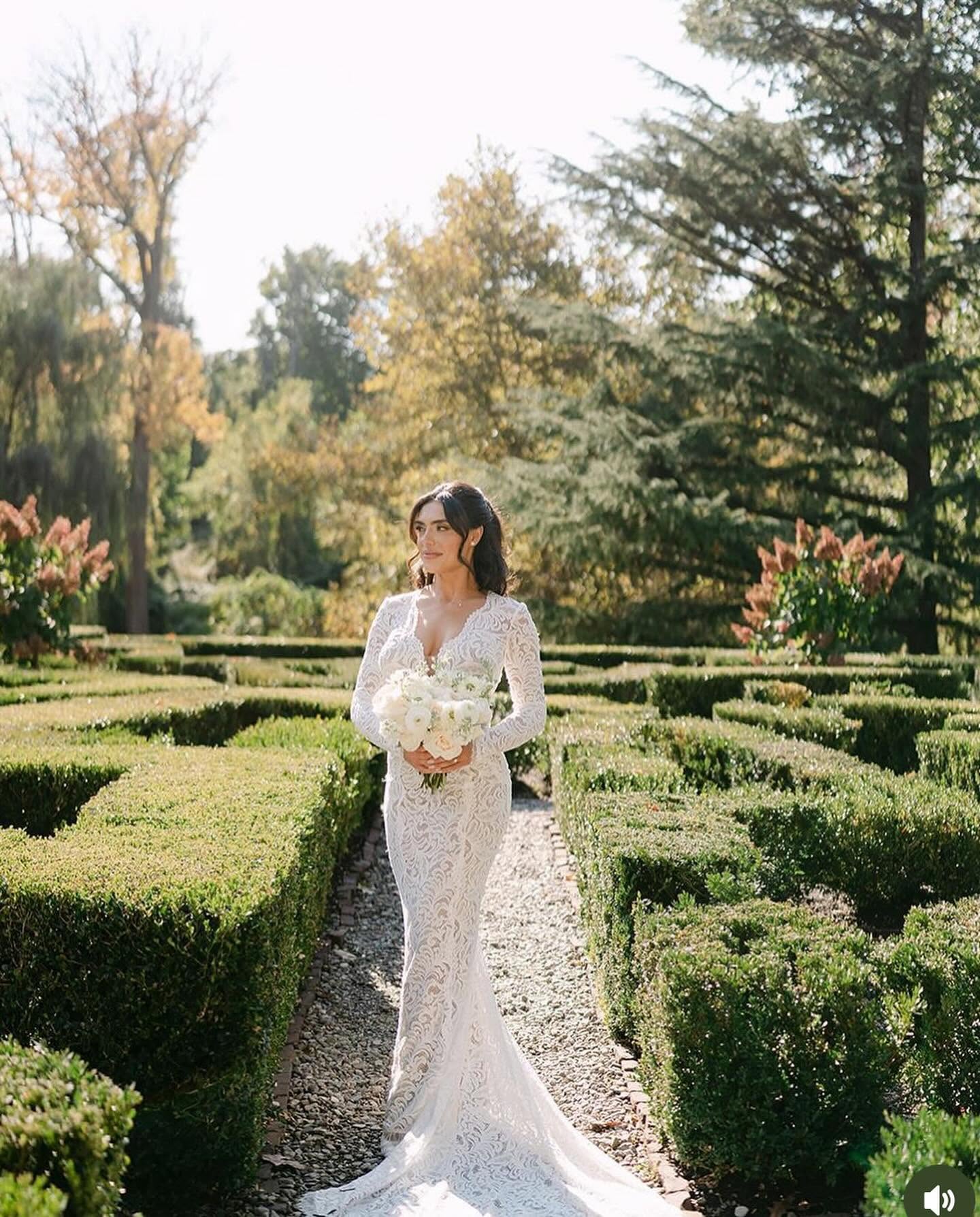 Bride in lace gown holding white bouquet in garden maze